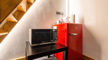 Una kitchenette con microondas, un refrigerador rojo y una mesa de madera.
