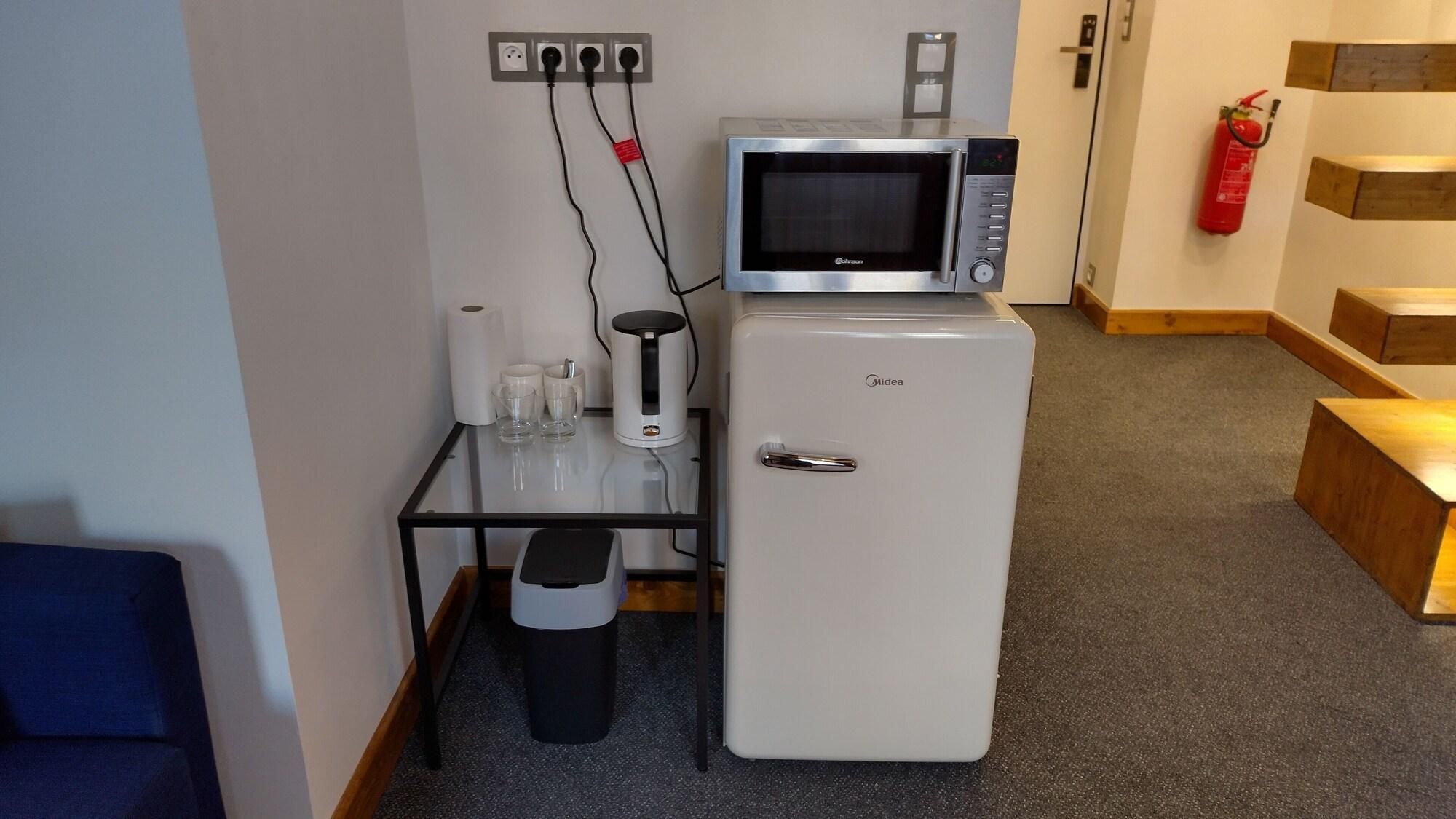 A compact kitchenette with a microwave, a small refrigerator, a coffee maker, and a trash bin.
