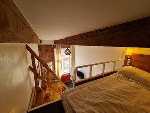 A bedroom with a wooden staircase, a bed, a nightstand with a lamp, and a view of the outside through a window. - Hotel S42 (Prague)