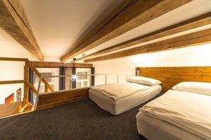 Una habitación con dos camas, techo de madera, ventana con cortinas y una escalera.