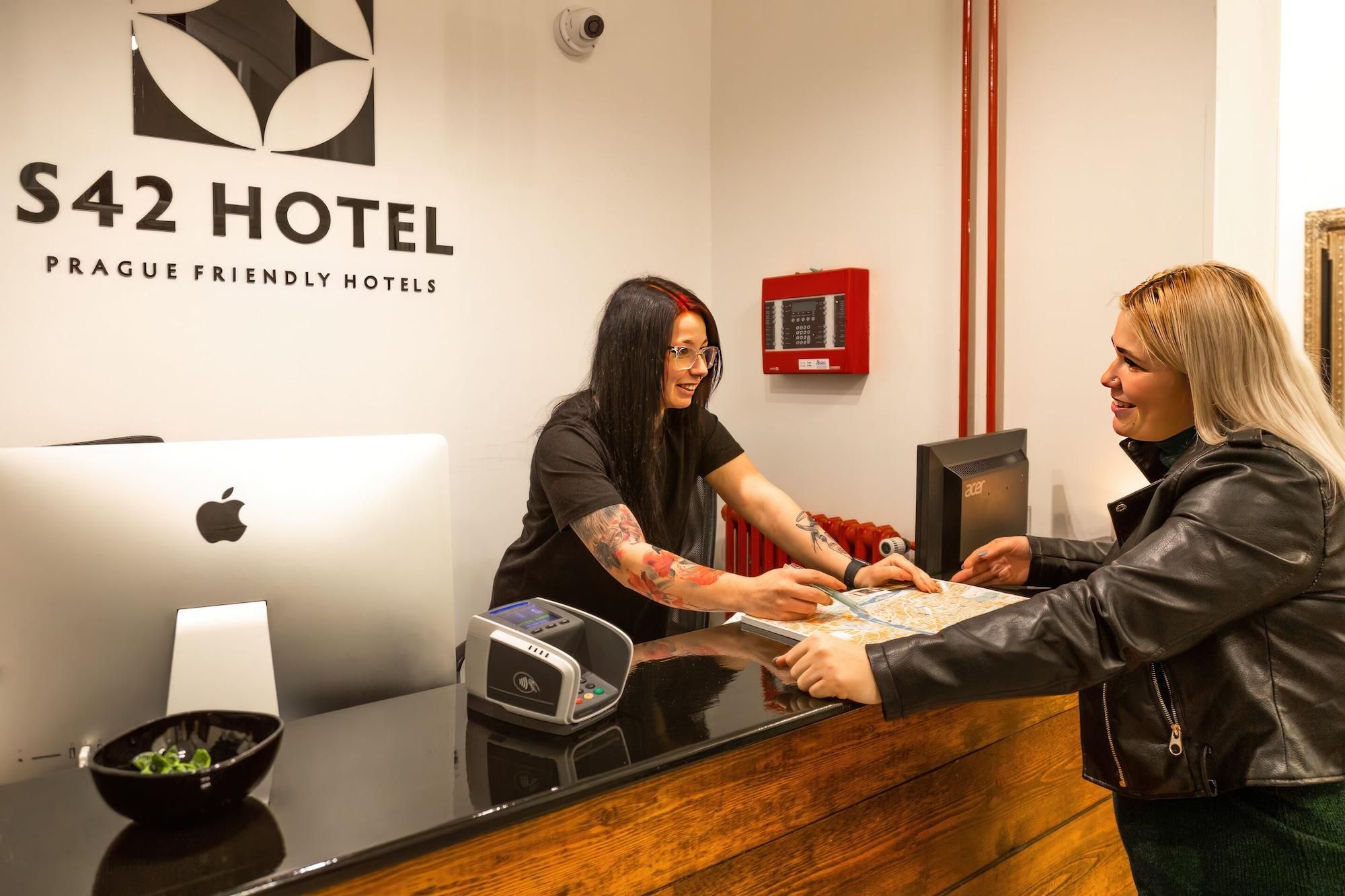 À l’hôtel S42, on peut voir un comptoir d’accueil équipé d’un terminal de paiement numérique, un saladier rempli de légumes verts et un détecteur d’incendie fixé au mur.