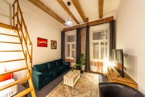 Una sala de estar con un sofá verde, una mesa de centro de madera, un mueble para televisor y una escalera.
