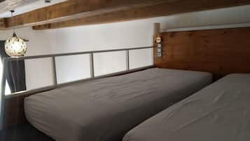 Una habitación con cama, ventana, techo de madera y una lámpara colgante.