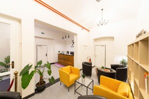 A hotel lobby with a reception desk, seating area with yellow and black chairs, a chandelier, and a bookshelf. - Hotel S42 (Prague)
