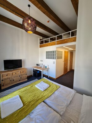 A hotel room with a bed, a TV, a desk with a computer, and a staircase leading to an upper level. - Hotel S42 (Prague)