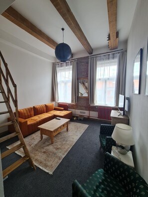 A living room with a wooden staircase, a sectional sofa, a coffee table, a patterned armchair, and a lamp. - Hotel S42 (Prague)