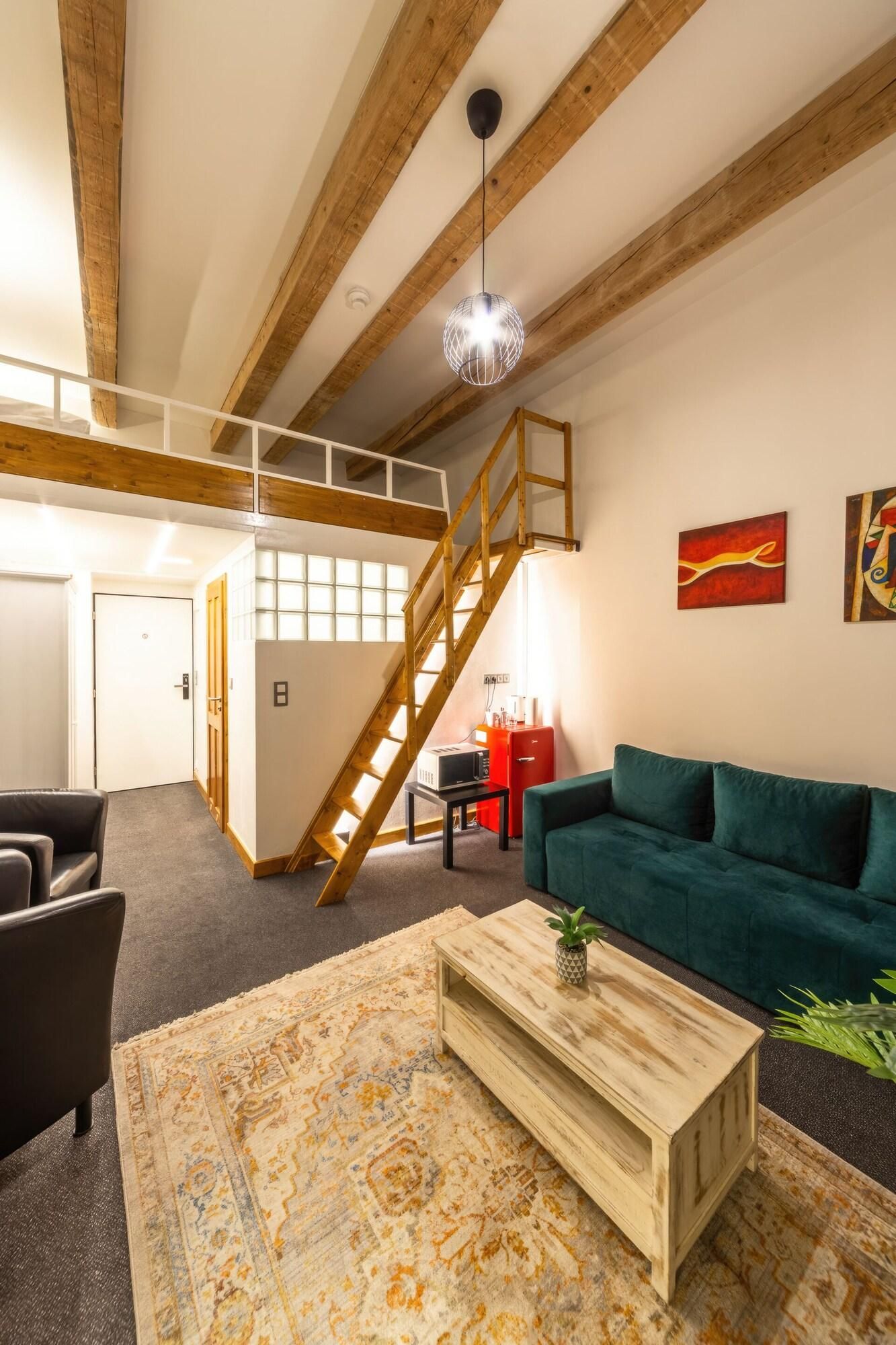 Un espacio habitable amplio con una escalera estilo loft, un sofá verde, una mesa de centro de madera y una alfombra estampada.