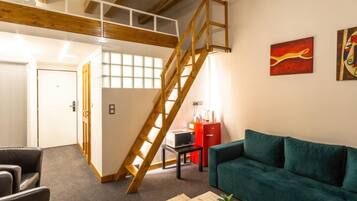 Un espacio habitable amplio con una escalera estilo loft, un sofá verde, una mesa de centro de madera y una alfombra estampada.