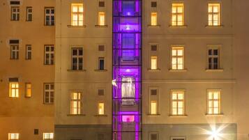 Un edificio de varios pisos con un hueco central para ascensor, múltiples ventanas en cada planta y un patio empedrado.