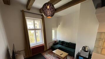 Una sala de estar con un sofá, una mesa de centro, una lámpara colgante, un radiador y una ventana con cortinas.