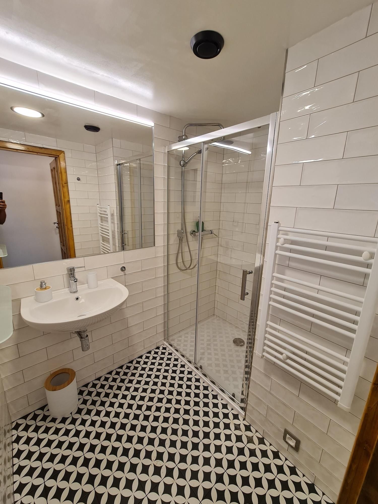 A bathroom with a white sink, mirror, shower, and a patterned floor.