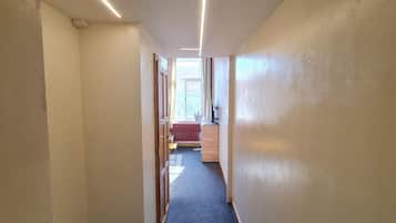 Un pasillo con pisos alfombrados, un radiador y una ventana con cortinas.
