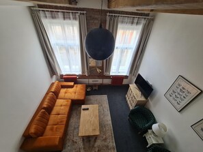 Una sala de estar con un sofá seccional, una mesa de centro, un televisor y un radiador.