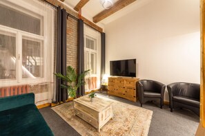 A living room with a television, two chairs, a wooden cabinet, a coffee table, and a plant. - Hotel S42 (Prague)