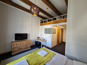 Habitación de hotel con cama, televisión, armario de madera, escritorio con microondas y lámpara colgante.