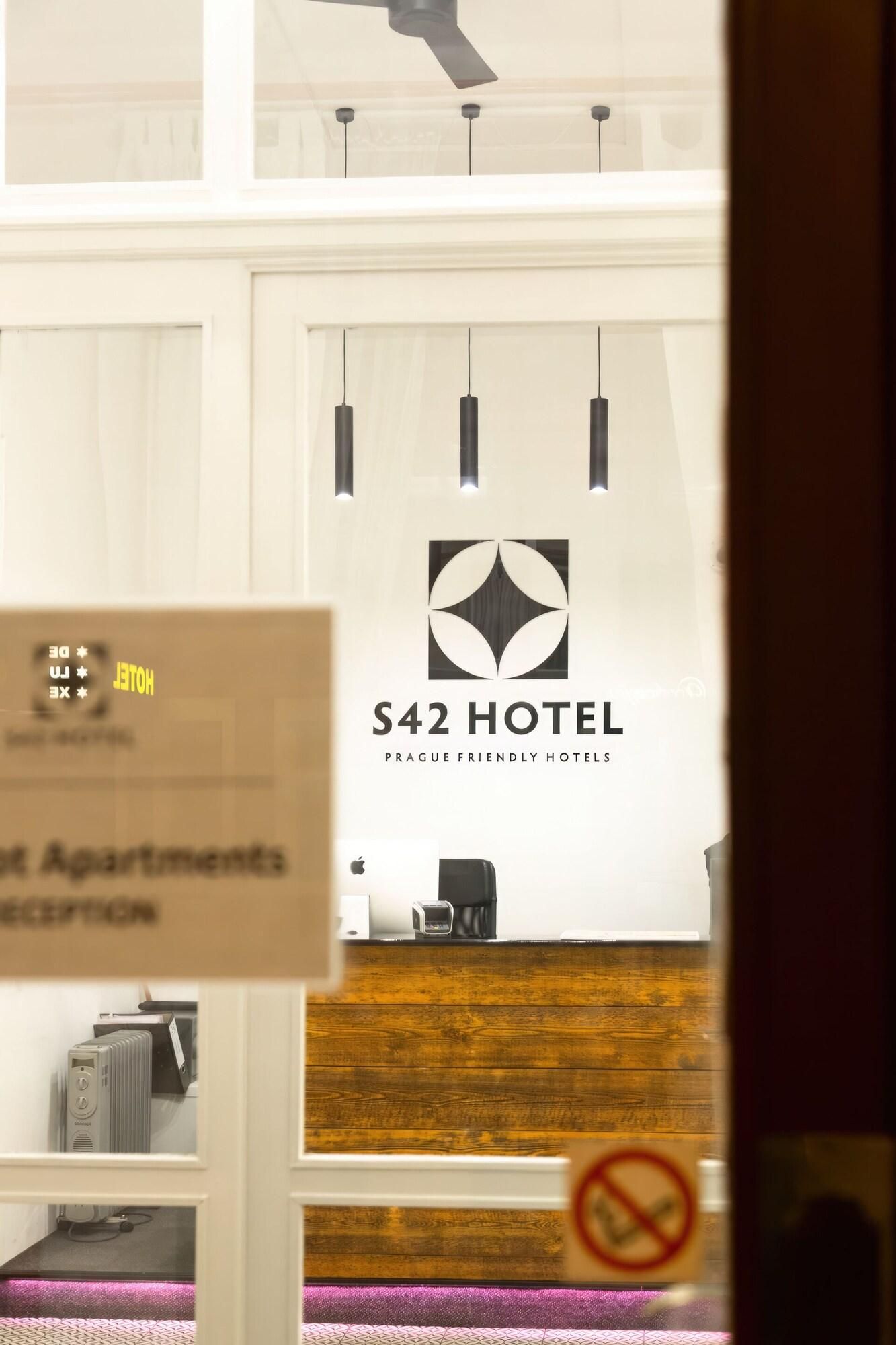 Zona de recepción con un cartel para el Hotel S42, un mostrador de madera y un letrero de prohibido fumar.