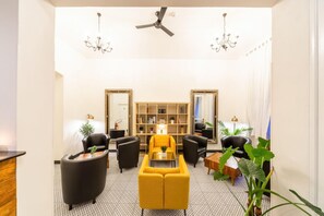 Una sala de estar moderna con un sofá amarillo, sillones negros, una estantería y un ventilador de techo.