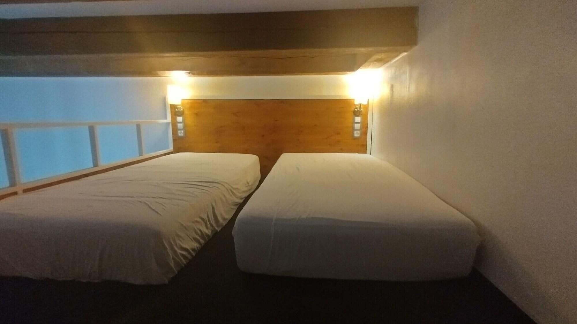 A room with two beds, wooden headboard, and a window with a view.