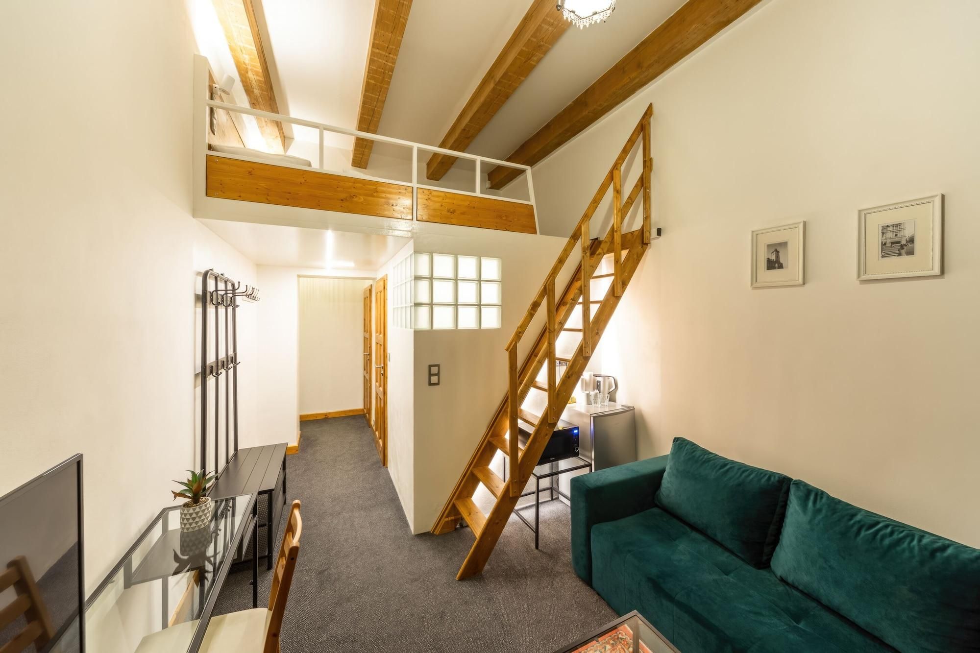 Un apartamento tipo loft con una escalera, un sofá verde, una mesa de centro y un televisor.