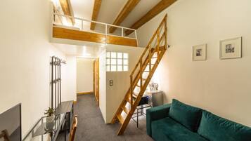 Un apartamento tipo loft con una escalera, un sofá verde, una mesa de centro y un televisor.