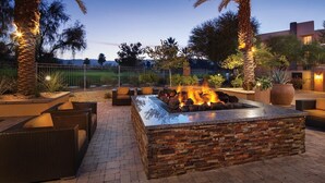 Une terrasse extérieure dotée d’un foyer en pierre, de meubles en osier et offrant une vue sur le paysage environnant.