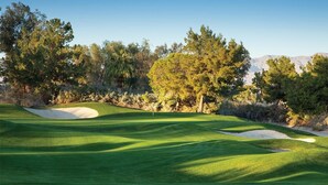 Un parcours de golf avec des bunkers de sable, des arbres et un ciel dégagé.