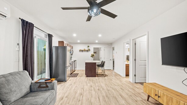 A modern living room with a grey sofa, a wooden cabinet, a ceiling fan, and a TV mounted on the wall. - New Duplex with King Bed and Easy Highway Access (Umatilla)