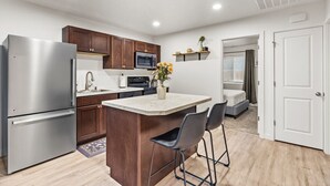 A modern kitchen with stainless steel appliances, wooden cabinets, a marble countertop, and a small bar area with two stools. - New Duplex with King Bed and Easy Highway Access (Umatilla)