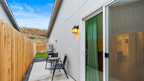 A patio with a table and chairs, a wooden fence, and a sliding glass door. - New Duplex with King Bed and Easy Highway Access (Umatilla)