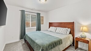 A neatly arranged bedroom with a bed, a bedside table with a lamp, and a window with curtains. - New Duplex with King Bed and Easy Highway Access (Umatilla)