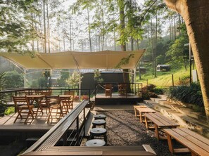 An outdoor seating area with tables and chairs, a covered seating area, and a view of the surrounding forest. - Bobocabin Pacet, Mojokerto (Pacet)