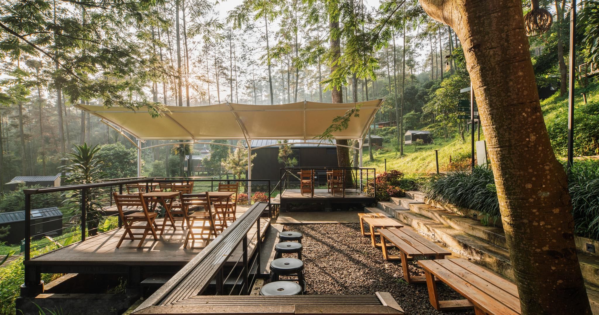 An outdoor seating area with tables and chairs, a covered section, and a view of the surrounding forest.