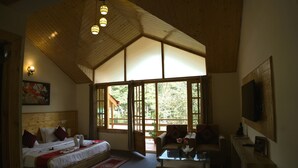 A bedroom with a large bed, a sofa, a coffee table, and a TV. There are windows and a wooden ceiling. - Persimmon Farmstead (Manali)