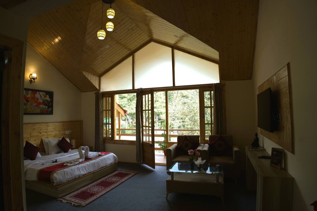 Une chambre avec un grand lit, un canapé, une table basse et un téléviseur. Il y a des fenêtres et un plafond en bois.