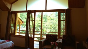 A room with a large window, a bed, a sofa, and a coffee table. - Persimmon Farmstead (Manali)