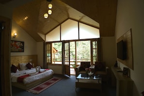 A bedroom with a large bed, a sofa, a coffee table, and a TV. There are windows and a wooden ceiling. - Persimmon Farmstead (Manali)