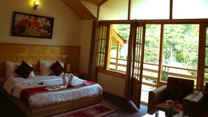 A bedroom with a large bed, a wooden ceiling, a painting on the wall, and a view through the window. - Persimmon Farmstead (Manali)