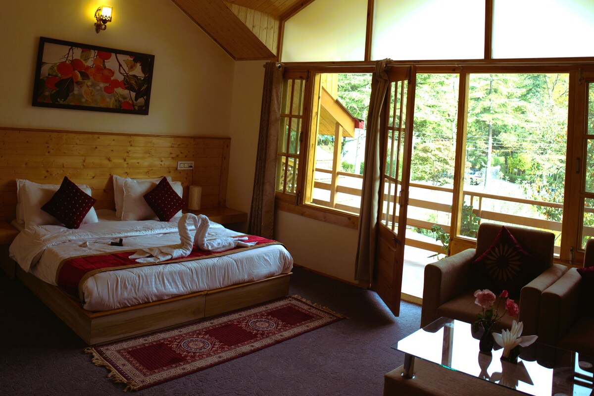 A bedroom with a large bed, a wooden ceiling, a painting on the wall, and a view through the window.