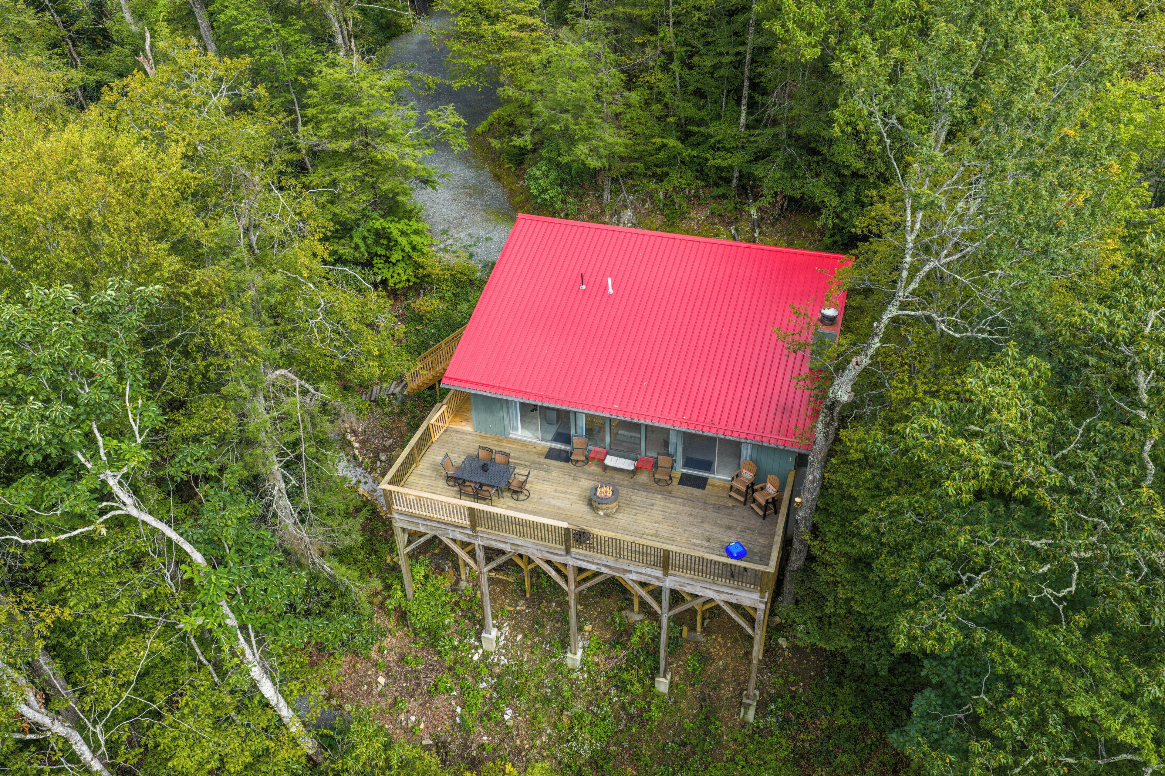 A wooden deck with outdoor furniture, a red roof, and a view of a forested area.