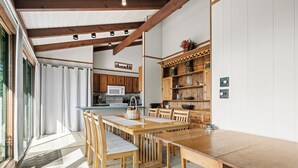 Ein Essbereich mit Holztisch und Stühlen, eine Küche im Hintergrund und ein großes Fenster mit Vorhängen.