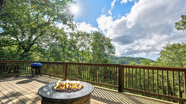 Eine Terrasse mit Feuerstelle und Grill, umgeben von einem Holzgeländer und mit Blick auf eine bewaldete Landschaft.