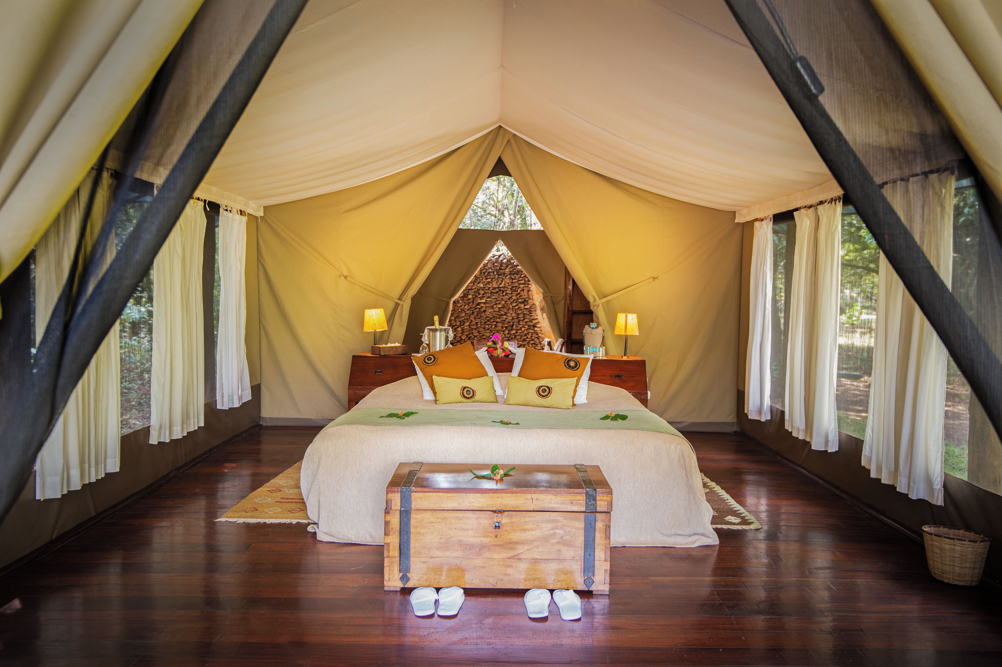 Una habitación con carpa, una cama grande, un banco de madera y dos lámparas de noche.