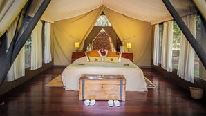Una habitación con carpa, una cama grande, un banco de madera y dos lámparas de noche.