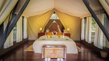 Una habitación con carpa, una cama grande, un banco de madera y dos lámparas de noche.