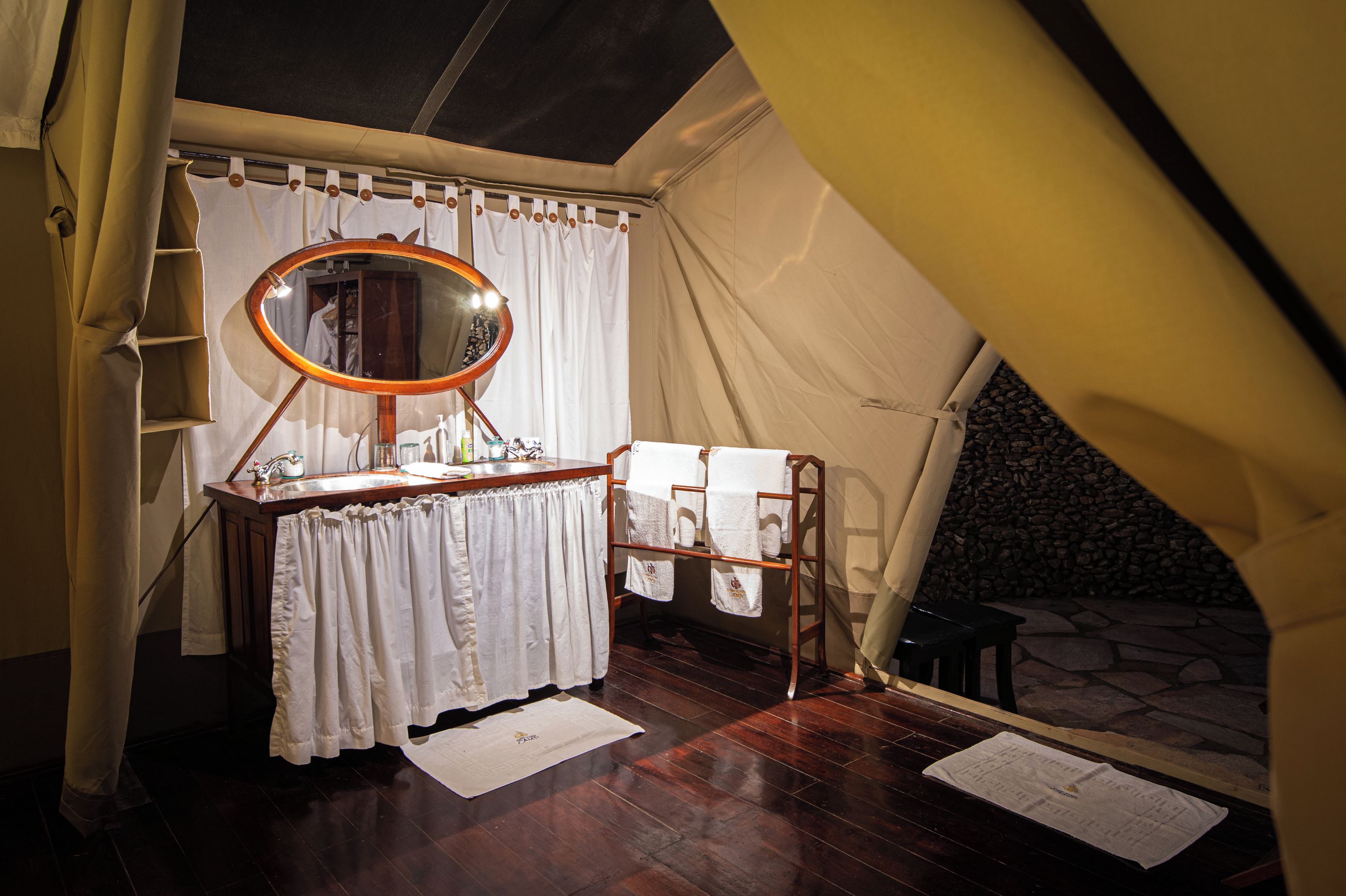 A tented room with a wooden vanity, a mirror, and a stone wall visible through the tent entrance.