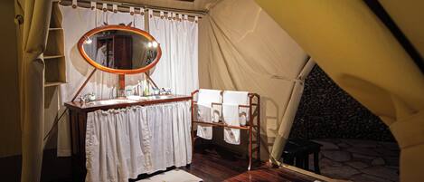 A tented room with a wooden vanity, a mirror, and a stone wall visible through the tent entrance.