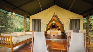 Eine Zelthütte mit einer Holzterrasse, einer Sitzecke, zwei Stühlen, einem Tisch und einem Bett mit Baldachin.