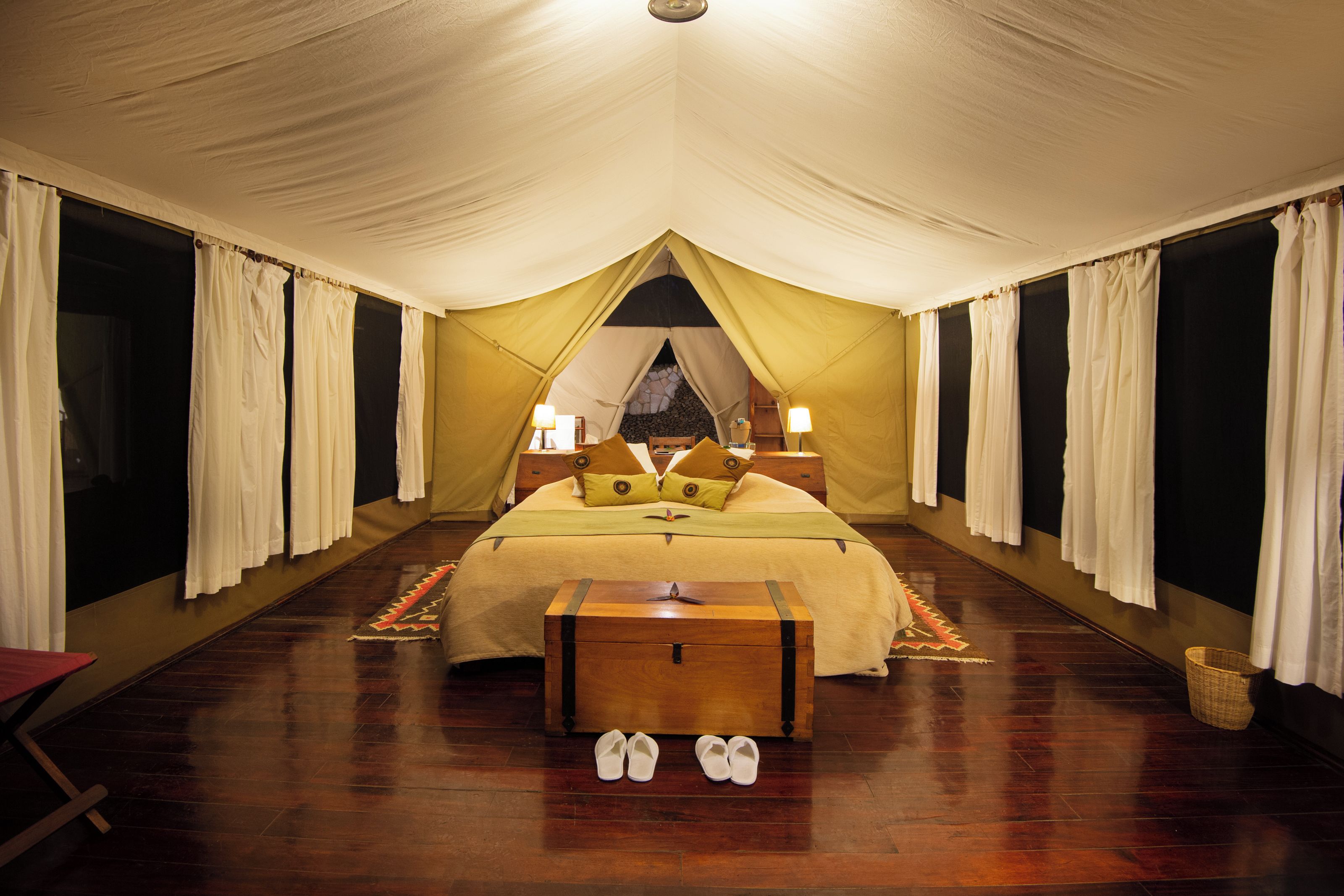 Una habitación con tienda de campaña, una cama, lámparas de noche, un cofre de madera y un par de zapatos en el suelo.