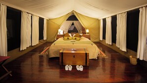 Una habitación con tienda de campaña, una cama, lámparas de noche, un cofre de madera y un par de zapatos en el suelo.