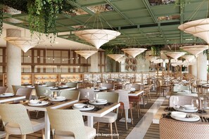 Een ruime restaurantruimte met hoge plafonds, hangplanten en diverse zithoeken.